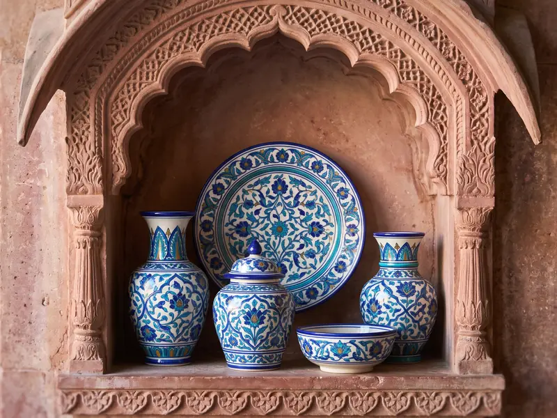 Jaipur blue pottery in a carved pink sandstone niche: two vases, a lidded jar, a bowl and a large plate painted with cobalt and turquoise flowers