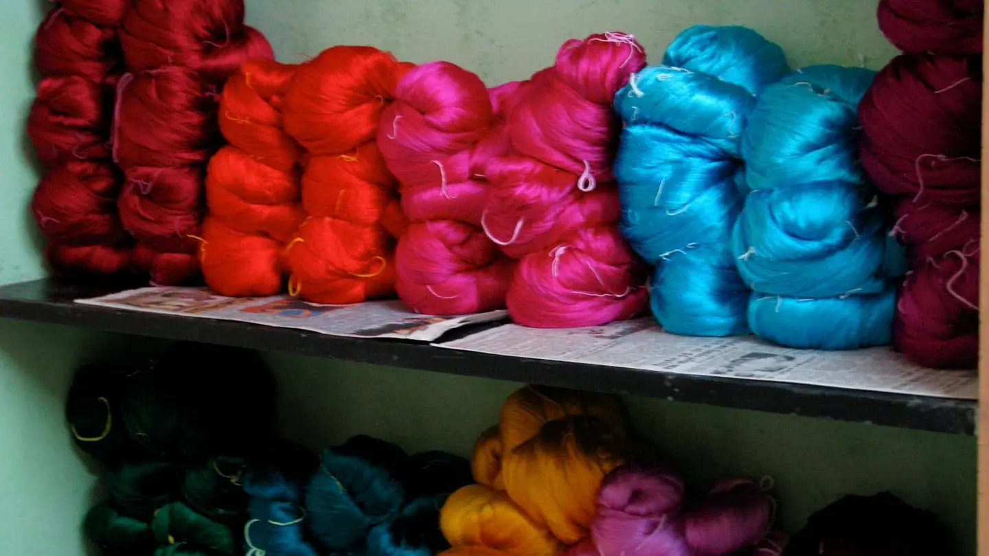 Skeins of dyed silk yarn in red, pink and turquoise stacked on a shelf